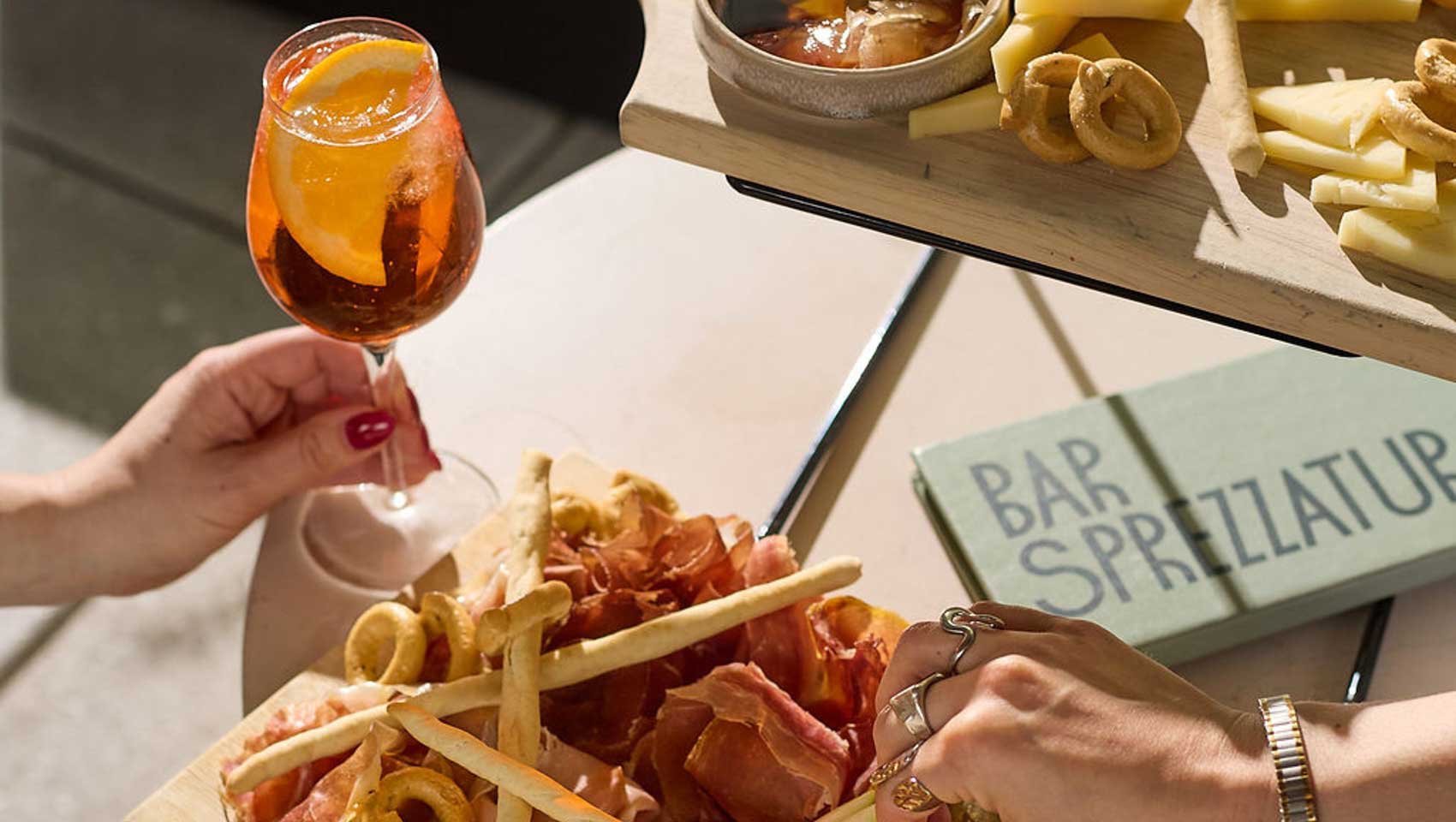 Charcuterie board with cured meats, cheeses, breadsticks, and an Aperol spritz