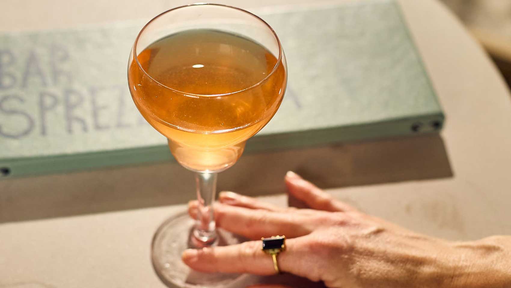 Amber cocktail served in a stemmed glass beside the Bar Sprezzatura menu