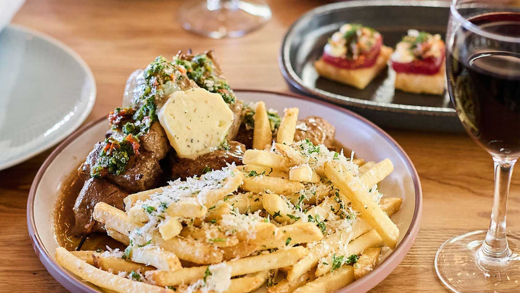 Steak frites with herb butter, Parmesan fries, and red wine at a restaurant table